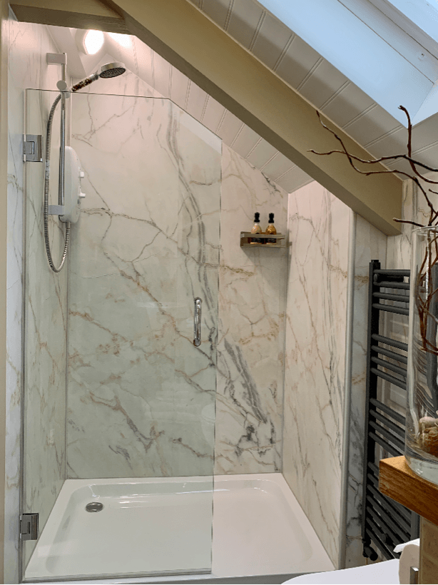 An angled shower with a clear glass shower screen and marble walls 