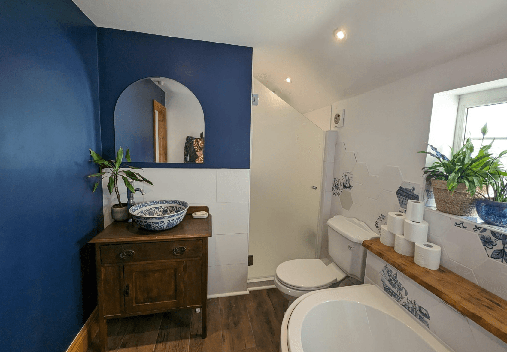 A bathroom with blue and white walls with a frosted glass shower screen and wooden flooring 