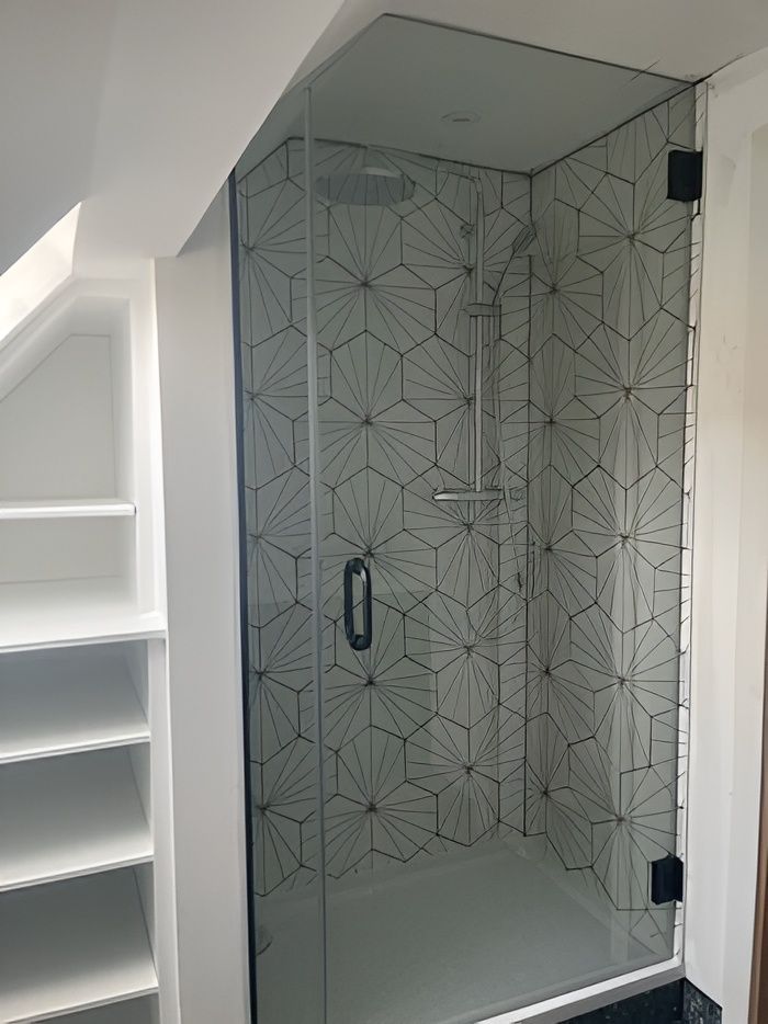 An alcove shower with a clear glass shower door and hexagonal-tiled walls