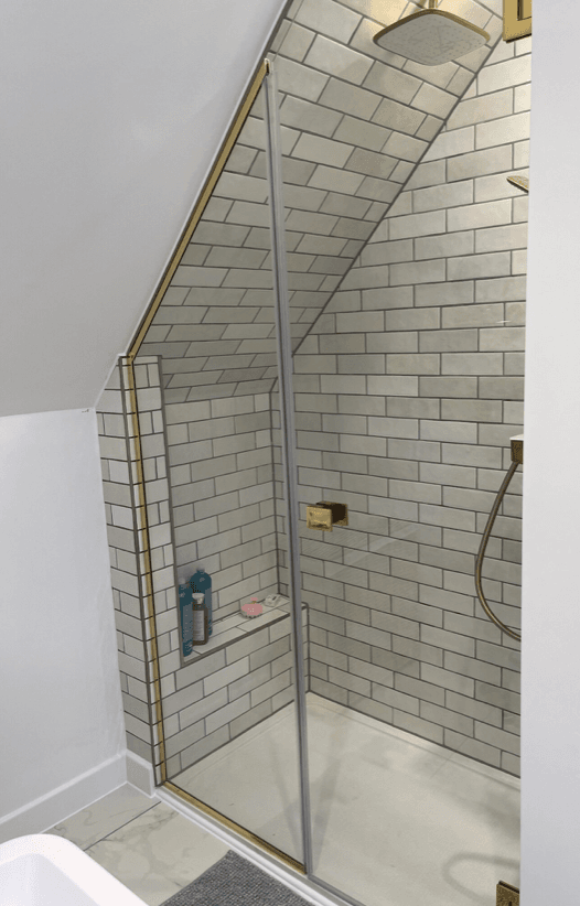 A slanted shower with a clear glass screen and white brick walls 